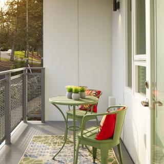 A cozy balcony with a small table and chairs, decorated with cushions and plants.