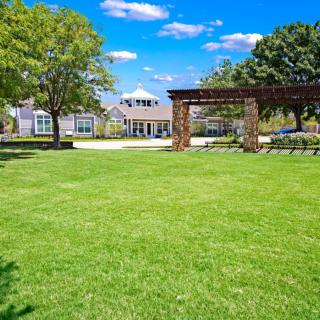 A beautiful garden with a lush green lawn and a house in the background under a clear blue sky.