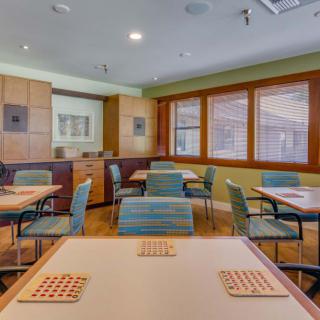 A cozy dining area with tables and chairs, featuring wooden floors and window blinds.