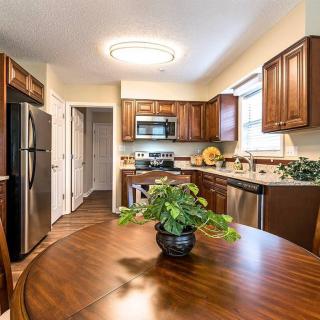 A modern kitchen with wooden cabinets, stainless steel appliances, and a dining table adorned with a potted plant.
