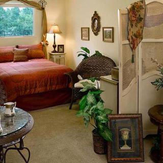A cozy bedroom with vintage decor and warm lighting, featuring a comfortable bed, plants, and artwork.