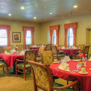 A cozy dining room with tables set for a meal, featuring red tablecloths and elegant chairs.