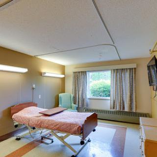 A patient room in a hospital featuring a bed, window with curtains, and basic furnishings.