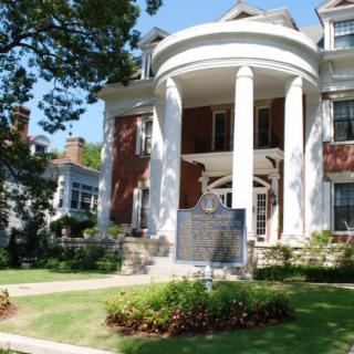 A historic building with large white columns and a commemorative plaque in the front yard.