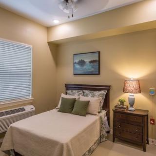 A cozy bedroom with a neatly made bed, a nightstand with a lamp, and wall artwork.