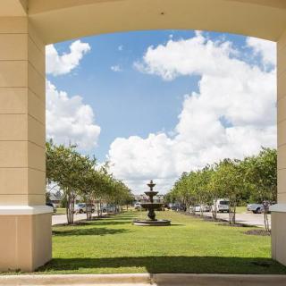 A scenic view through an archway featuring a fountain surrounded by trees and a partly cloudy sky.
