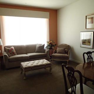 A cozy living room with a sofa, armchair, and a coffee table, featuring a dining area and wall art.