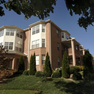 A multi-story apartment building with a brick exterior, surrounded by well-maintained landscaping and trees.