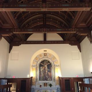 An interior view of a church featuring a wooden ceiling and an ornate altar.