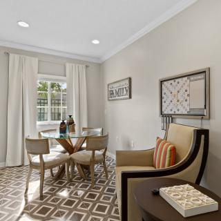 A modern dining room featuring a geometric patterned rug, a glass-top table with chairs, decorative wall art, and bright natural lighting.