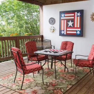 An inviting outdoor patio with a table and red cushioned chairs, accented by patriotic artwork on the wall.