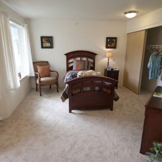 A cozy bedroom with a single bed, a chair by the window, and an open closet.