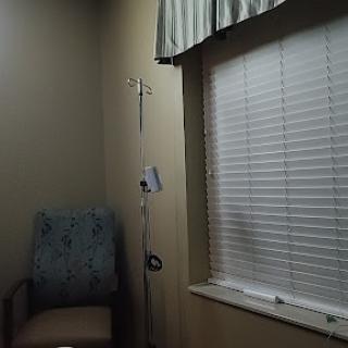 A tranquil hospital room featuring a patient chair and an intravenous pole beside a window with blinds.