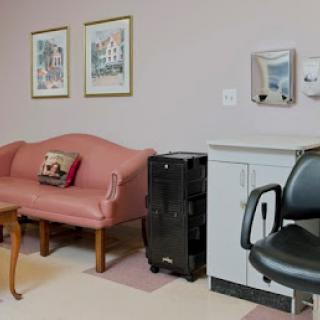 A waiting room featuring a pink sofa, a black chair, and framed artwork on the walls.