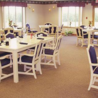 A cozy dining room with tables and chairs arranged neatly, featuring large windows that allow natural light to enter.