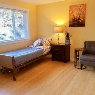 A cozy bedroom with a single bed, nightstand, lamp, and chair on a wooden floor.