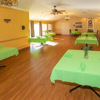 A spacious dining room with green tablecloths and wooden flooring.