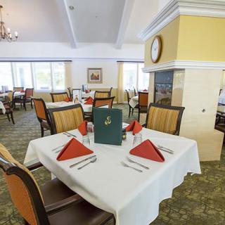 A formal dining area with elegantly set tables, featuring red napkins and a menu in a bright, inviting atmosphere.