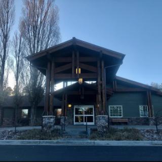 A modern wooden building with a distinctive architectural design, surrounded by trees.