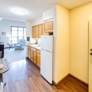 A cozy apartment interior featuring a compact kitchen with wooden cabinets and a fridge, leading into a bright living area.