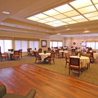 An empty dining room with tables and chairs arranged neatly, featuring both carpeted and wooden flooring.