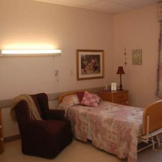 A cozy hospital room featuring a single bed, an armchair, and wall art.