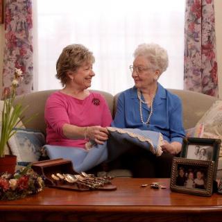 Two elderly women sit on a couch, sharing a warm conversation in a cozy living room.