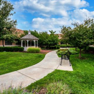 A serene garden with a curved pathway leading to a gazebo, surrounded by lush greenery and trees.