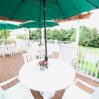 A serene outdoor patio with white furniture and green umbrellas overlooking a lush garden.