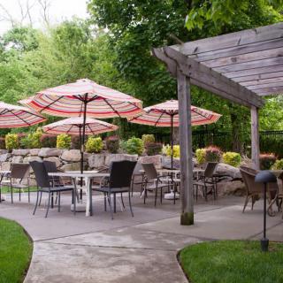 An inviting outdoor patio space with seating, umbrellas, and a pergola surrounded by greenery.
