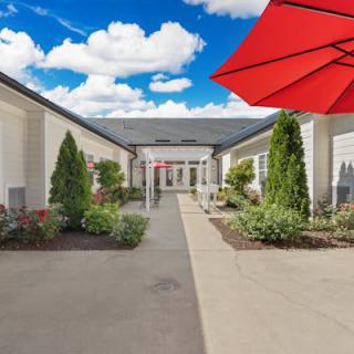 A landscaped pathway between buildings, featuring greenery and a bright red umbrella.