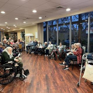 A group of elderly individuals in wheelchairs gathered in a nursing home's community room.