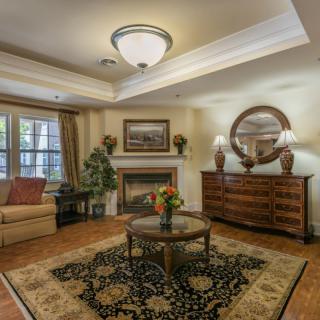 A traditional living room with classic furnishings and a fireplace, featuring a patterned rug and elegant lighting.