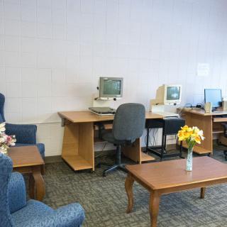 An office space with vintage computers, desks, chairs, and a vase of flowers on a table.