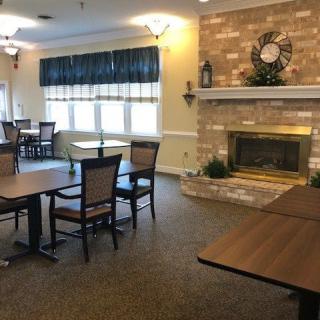 A cozy dining area with tables and chairs, featuring a brick fireplace and large windows.