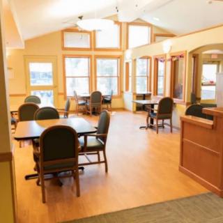 A brightly lit dining area with several tables and chairs, featuring large windows allowing natural light to fill the space.