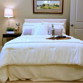 A cozy bedroom setup featuring a neatly made bed with white linens, flanked by a modern lamp and a framed artwork on the wall.