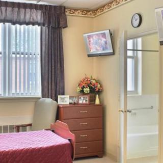 A well-organized hospital room with a bed, dresser, wall-mounted television, and a window with curtains.