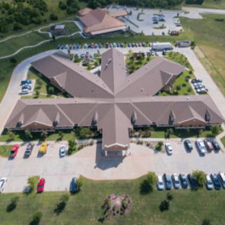 An aerial view of a uniquely designed building with a surrounding parking lot and landscaped area.