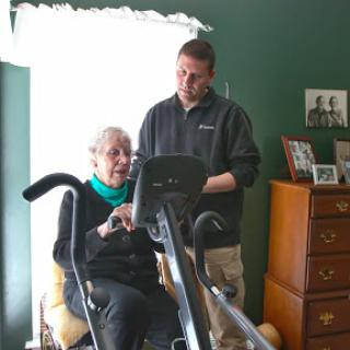 A caregiver assisting an elderly woman with her exercise routine in a cozy home setting.