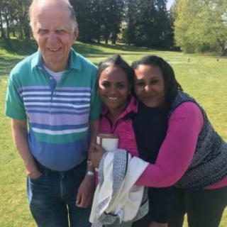 A group of three people smiling and posing together outdoors on a sunny day.