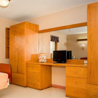 A cozy hotel room featuring wooden furniture, including a wardrobe and a desk with a television.