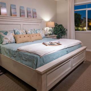 A cozy and well-decorated bedroom with a large bed, stylish pillows, a nightstand with a lamp, and a window overlooking the outdoors.