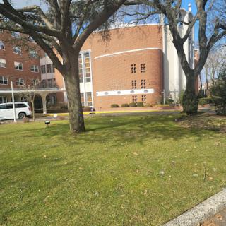 A view of a brick building surrounded by greenery and trees on a sunny day.