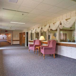 A quiet corridor with two pink armchairs and a lamp against a row of windows adorned with drapes.