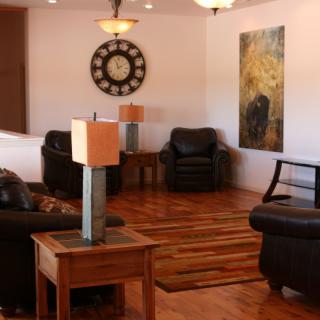 A cozy living room featuring leather chairs, wooden flooring, stylish table lamps, a large wall clock, and modern artwork.