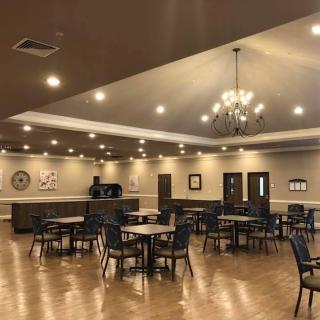 A spacious dining hall with chandeliers, wooden flooring, and neatly arranged tables and chairs.