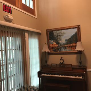 A room featuring a piano with a painting above it, flanked by two lamps, and an exit sign nearby.