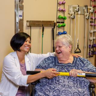 A healthcare professional shares a joyful moment with an elderly woman during a rehabilitation session.
