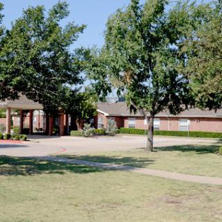 A serene view of a school surrounded by green lawns and trees under a clear blue sky.